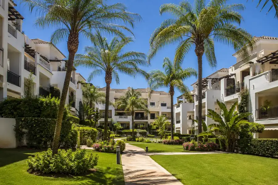 Zonas comunes ajardinadas con palmeras y piscina en una urbanización premium